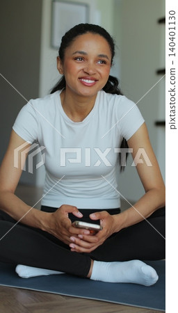 Vertical Video. Portrait of a sporty woman resting at home after training and using her smartphone. Beautiful healthy sportive girl athlete resting after intense hard training. Vertical Video. Portrait of a sporty woman resting at home after training and using her smartphone. Beautiful healthy sportive girl athlete resting after intense hard training. 140401130