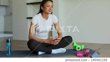 Young woman resting at home after training and using her smartphone. Beautiful healthy sportive girl athlete resting after intense hard training. 140401166