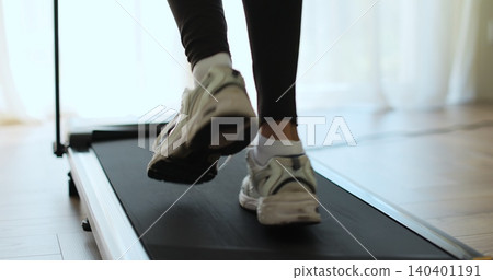 Closeup of a woman legs running on a treadmill at home. Back view of legs having workout on treadmill. Closeup of a woman legs running on a treadmill at home. Back view of legs having workout on treadmill. 140401191