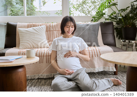 一位孕婦坐在客廳地板上,輕輕撫摸自己的肚子。 一位孕婦坐在客廳地板上,輕輕撫摸自己的肚子。 140401389