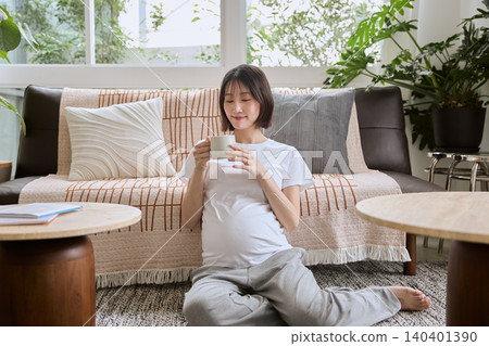 一位孕婦坐在客廳地板上,手裡拿著一個杯子。 一位孕婦坐在客廳地板上,手裡拿著一個杯子。 140401390