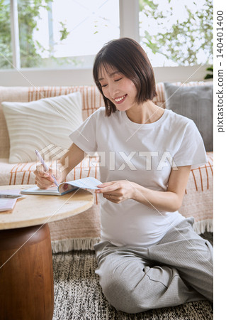 一位孕婦在客廳沙發上放鬆休息,同時在她的母嬰健康手冊上做筆記。 一位孕婦在客廳沙發上放鬆休息,同時在她的母嬰健康手冊上做筆記。 140401400