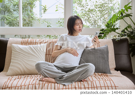 一位孕婦坐在沙發上看著她的智慧型手機。 一位孕婦坐在沙發上看著她的智慧型手機。 140401410