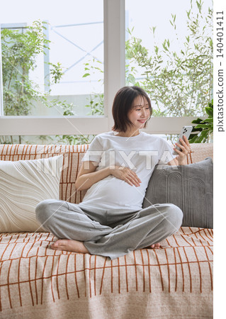 A pregnant woman sits on a sofa, looking at her smartphone and smiling. A pregnant woman sits on a sofa, looking at her smartphone and smiling. 140401411