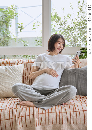 一位孕婦正放鬆地躺在沙發上,看著她的智慧型手機。 一位孕婦正放鬆地躺在沙發上,看著她的智慧型手機。 140401412