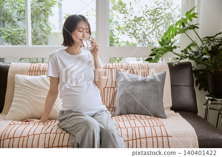 一位孕婦坐在沙發上喝水。 一位孕婦坐在沙發上喝水。 140401422