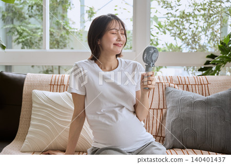 A pregnant woman cooling herself with a handheld fan. A pregnant woman cooling herself with a handheld fan. 140401437