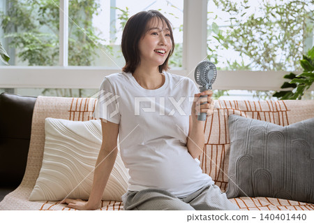 A pregnant woman cooling herself with a handheld fan. A pregnant woman cooling herself with a handheld fan. 140401440