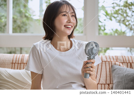 A young pregnant woman smiling and holding a portable fan on the living room sofa. A young pregnant woman smiling and holding a portable fan on the living room sofa. 140401441