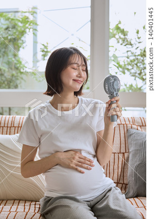 A pregnant woman cools herself with a portable fan in the hot summer. A pregnant woman cools herself with a portable fan in the hot summer. 140401445