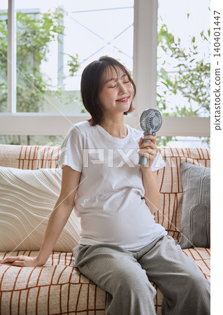 一位年輕女子在沙發上用手持風扇為自己降溫。 一位年輕女子在沙發上用手持風扇為自己降溫。 140401447