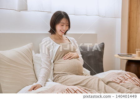 一位孕婦躺在床上,手撫著肚子,面帶微笑。 一位孕婦躺在床上,手撫著肚子,面帶微笑。 140401449