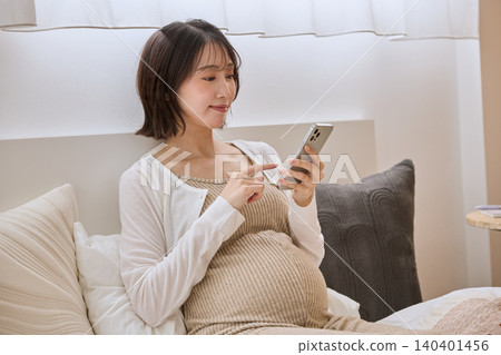 A pregnant woman using her smartphone in bed A pregnant woman using her smartphone in bed 140401456