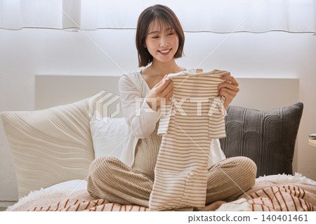 A pregnant woman smiles as she holds baby clothes in her hand while lying in bed. A pregnant woman smiles as she holds baby clothes in her hand while lying in bed. 140401461