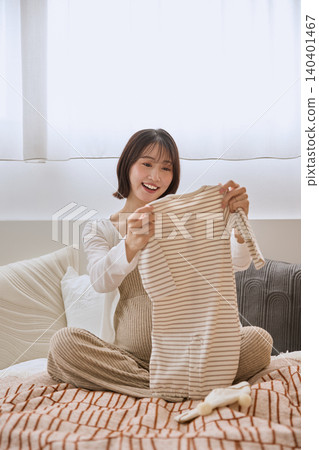 一位年輕女子麵帶微笑地撿起床上的嬰兒衣服。 一位年輕女子麵帶微笑地撿起床上的嬰兒衣服。 140401467