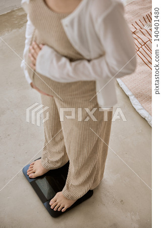 一位女士正在體重計上稱重,她的雙腳清晰可見。 一位女士正在體重計上稱重,她的雙腳清晰可見。 140401480