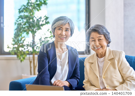 一位女顧問和一位資深女性坐在沙發上對著鏡頭微笑。 140401709