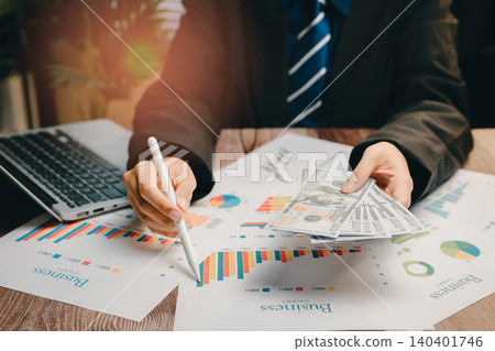Businessman Analyzing Financial Data with Graphs, Cash, and Laptop in Modern Office Environment, Business concept Businessman Analyzing Financial Data with Graphs, Cash, and Laptop in Modern Office Environment, Business concept 140401746