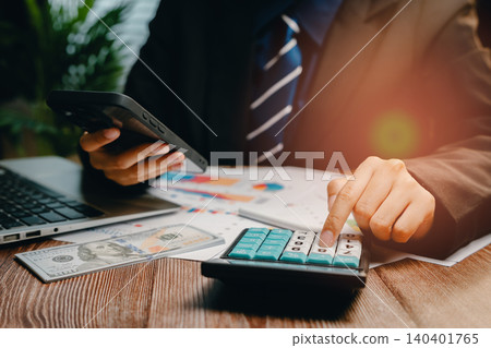 Businessman Using Calculator and Smartphone for Financial Analysis with Charts and Money, Business concept 140401765