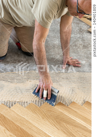 Worker applying parquet flooring adhesive with notched trowel during home construction, top view Worker applying parquet flooring adhesive with notched trowel during home construction, top view 140401809