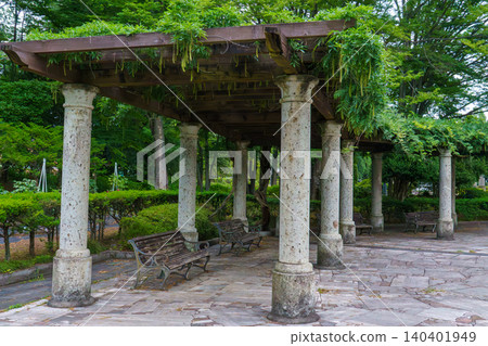 A wisteria trellis made of Oya stone at the entrance to a lush green park. A wisteria trellis made of Oya stone at the entrance to a lush green park. 140401949