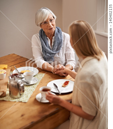 Mother, daughter and home with holding hands in table on lunch for bonding, support and visit. House, family and tea with food for conversation on break, leisure and happiness for coffee and care. Mother, daughter and home with holding hands in table on lunch for bonding, support and visit. House, family and tea with food for conversation on break, leisure and happiness for coffee and care. 140402135