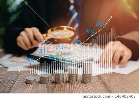 Business professional analyzing financial growth trends with magnifying glass and coins on a wooden table, Business concept 140402402