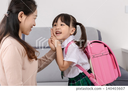 A caring mother gently touching her happy daughter's cheek as they share a warm conversation before the school day. 140403607
