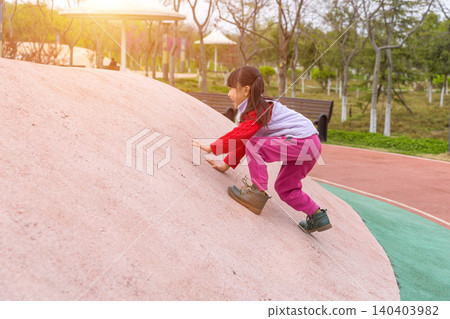a happy little girl in a red sweater crawls on a slope of the playground. a happy little girl in a red sweater crawls on a slope of the playground. 140403982