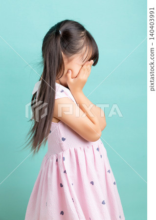 Side view of a crying little girl covering her face with her hands, showing grief or shame. Side view of a crying little girl covering her face with her hands, showing grief or shame. 140403991