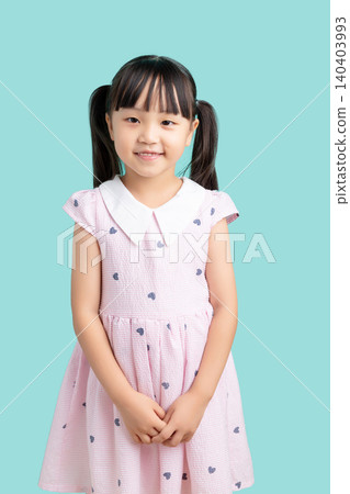 Portrait of a happy smiling little girl standing politely against a solid blue background. Portrait of a happy smiling little girl standing politely against a solid blue background. 140403993