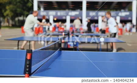 Ping pong net on blue table with blurred people playing tabletop tennis outdoors Ping pong net on blue table with blurred people playing tabletop tennis outdoors 140404234