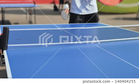 Adult playing table tennis outdoors, holding paddle hitting ping pong ball over net Adult playing table tennis outdoors, holding paddle hitting ping pong ball over net 140404255