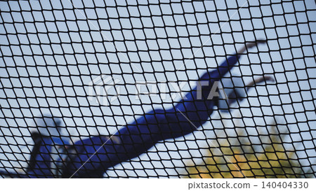 Person jumping on trampoline seen through safety net against blue sky 140404330