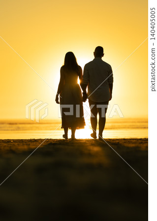 Couple walks hand in hand on the beach at sunset near the water on a warm evening Couple walks hand in hand on the beach at sunset near the water on a warm evening 140405005