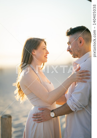 Couple sharing a moment on the beach during sunset near water in a warm evening light at a seaside location Couple sharing a moment on the beach during sunset near water in a warm evening light at a seaside location 140405038