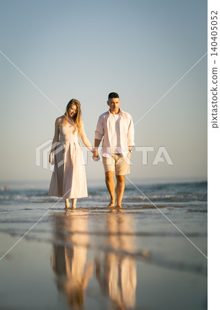 Couple walks on the beach holding hands during sunset near the ocean with footprints in the sand Couple walks on the beach holding hands during sunset near the ocean with footprints in the sand 140405052
