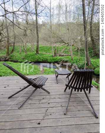 Wooden terrace with lounge chairs by a forest stream. Wooden terrace with lounge chairs by a forest stream. 140405502