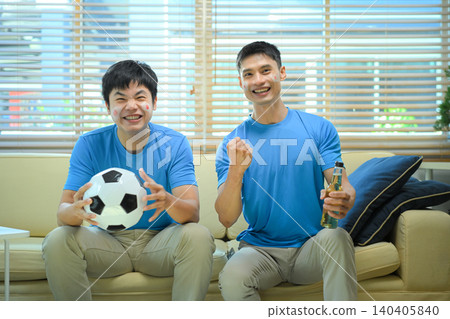 Friends celebrating soccer win at home, mens cheer on sofa after goal Friends celebrating soccer win at home, mens cheer on sofa after goal 140405840
