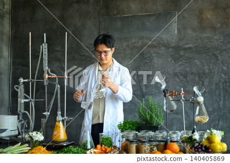 Young Asian Scientist in Lab Coat Conducting Herbal Extraction Research with Fresh Botanicals and Glass Laboratory Equipment 140405869