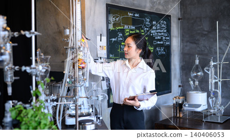 Young Asian Female Scientist Working with Distillation Equipment in Modern Laboratory with Chalkboard Young Asian Female Scientist Working with Distillation Equipment in Modern Laboratory with Chalkboard 140406053