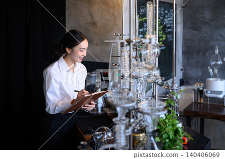 Young Asian Woman Scientist Taking Notes on Clipboard Beside Glass Distillation Equipment in Laboratory Young Asian Woman Scientist Taking Notes on Clipboard Beside Glass Distillation Equipment in Laboratory 140406069
