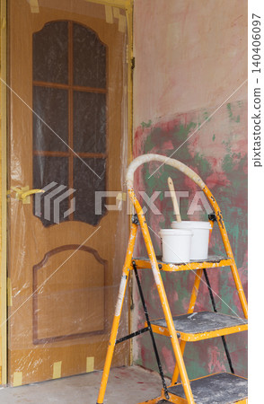 Home renovation and interior painting project with yellow stepladder, paint buckets, and brush in room under refurbishment. Wooden door protected with plastic sheeting and masking tape Home renovation and interior painting project with yellow stepladder, paint buckets, and brush in room under refurbishment. Wooden door protected with plastic sheeting and masking tape 140406097