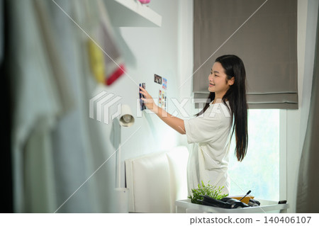 Young Asian Female Student Decorating Dorm Room Wall with Photos While Moving Into University Accommodation Young Asian Female Student Decorating Dorm Room Wall with Photos While Moving Into University Accommodation 140406107