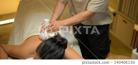 Relaxed woman receiving traditional herbal compress massage in a serene spa Relaxed woman receiving traditional herbal compress massage in a serene spa 140406130
