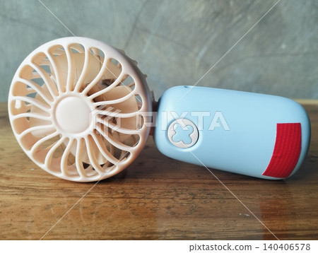 Compact Mini Electric Fan for Personal Cooling on a wooden table Compact Mini Electric Fan for Personal Cooling on a wooden table 140406578