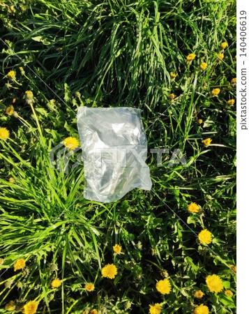 Plastic bag on lush green grass surrounded by yellow dandelions in a sunny park Plastic bag on lush green grass surrounded by yellow dandelions in a sunny park 140406619
