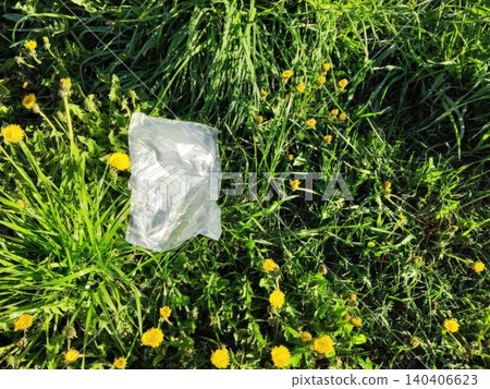 Plastic bag litter on lush green grass among vibrant yellow dandelions in nature Plastic bag litter on lush green grass among vibrant yellow dandelions in nature 140406623