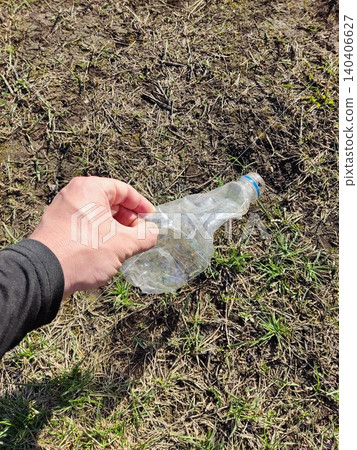 Hand picking up plastic bottle from grass to promote environmental cleanup Hand picking up plastic bottle from grass to promote environmental cleanup 140406627