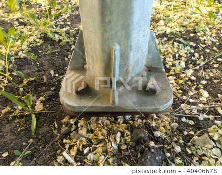 Base of metal pole secured with bolts in outdoor setting with fallen petals Base of metal pole secured with bolts in outdoor setting with fallen petals 140406678